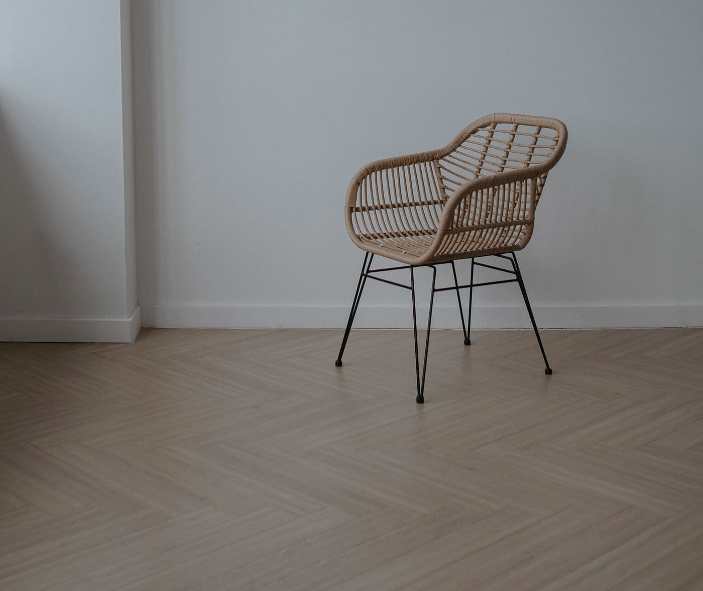 Parquet à bâtons rompus en chêne pâle, une chaise en rotin contre un mur blanc